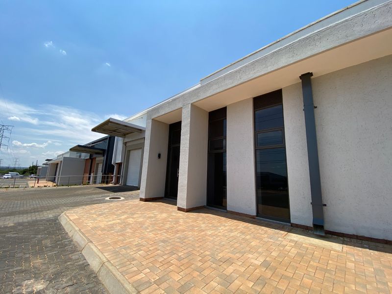Modern industrial unit exterior featuring a paved driveway, roller shutter door, and clean architectural lines with large aluminium-framed windows.