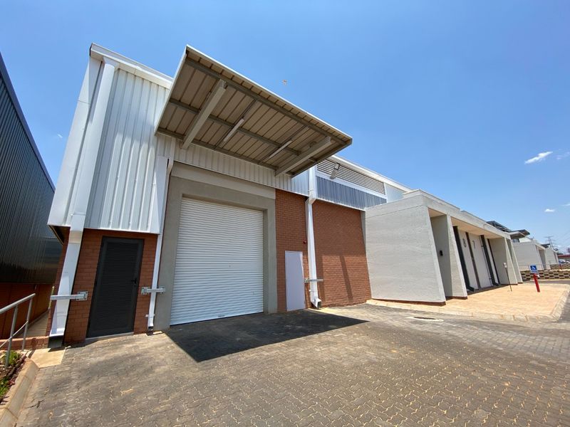 Modern industrial unit featuring a large roller shutter door, metal cladding, brick facade, and a paved driveway with a covered loading canopy.