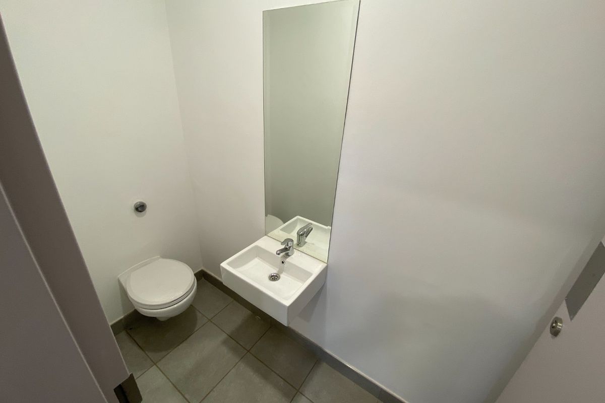 A clean, minimalist industrial-style powder room featuring a wall-mounted basin, chrome mixer tap, wall-mounted toilet, and neutral tiled flooring.