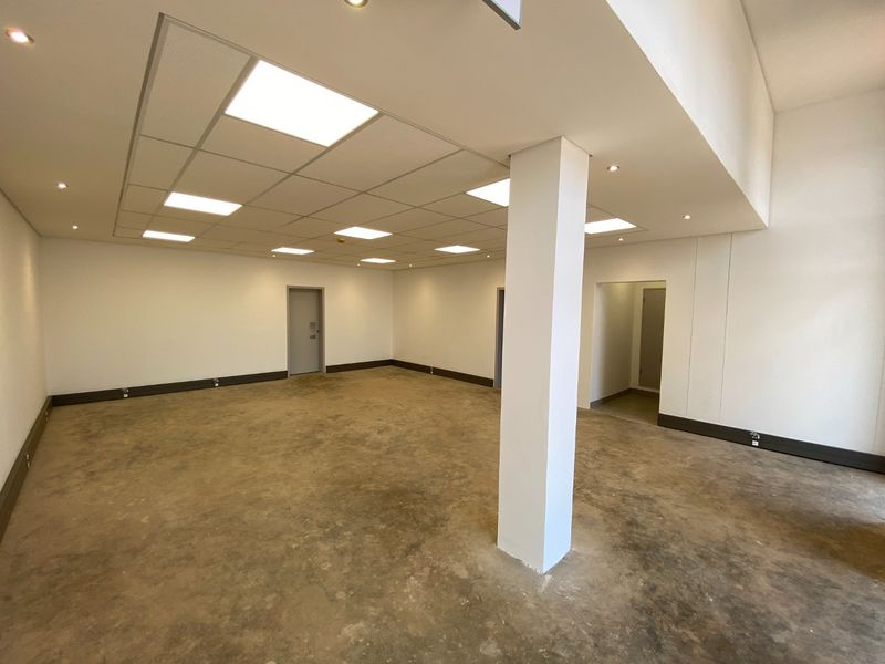 Spacious open-plan industrial office area featuring a suspended ceiling, recessed lighting, and a central structural column with unfinished concrete flooring.