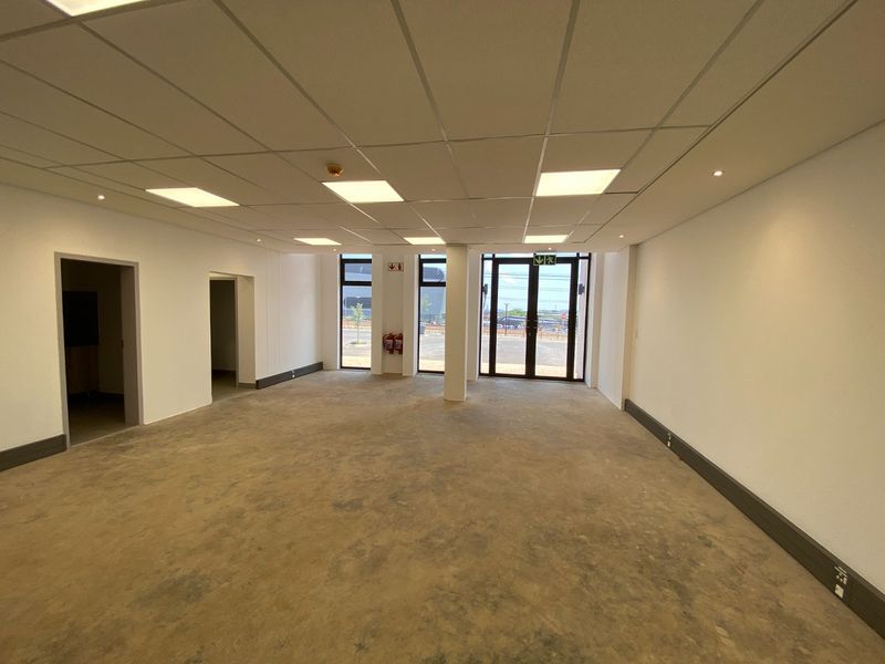 An open-plan industrial office space featuring a suspended ceiling, recessed lighting, and large glass entrance doors, ready for custom flooring and fit-out.