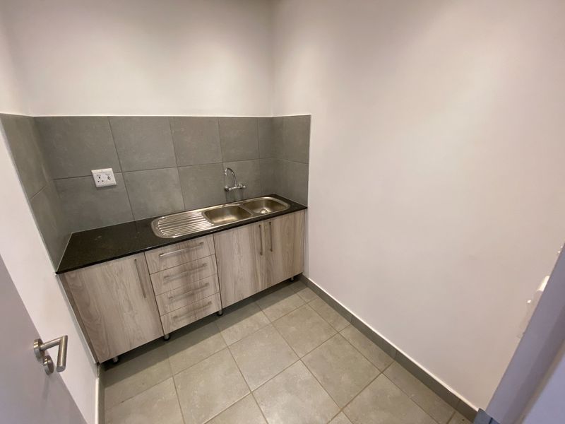 A clean, modern scullery area featuring built-in cabinetry, a stainless steel sink, stone countertop, and neutral tiled finishes.