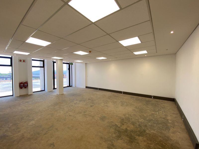 A spacious, empty industrial office unit featuring a suspended ceiling with recessed LED lighting, large windows, and concrete flooring with integrated electrical outlets.