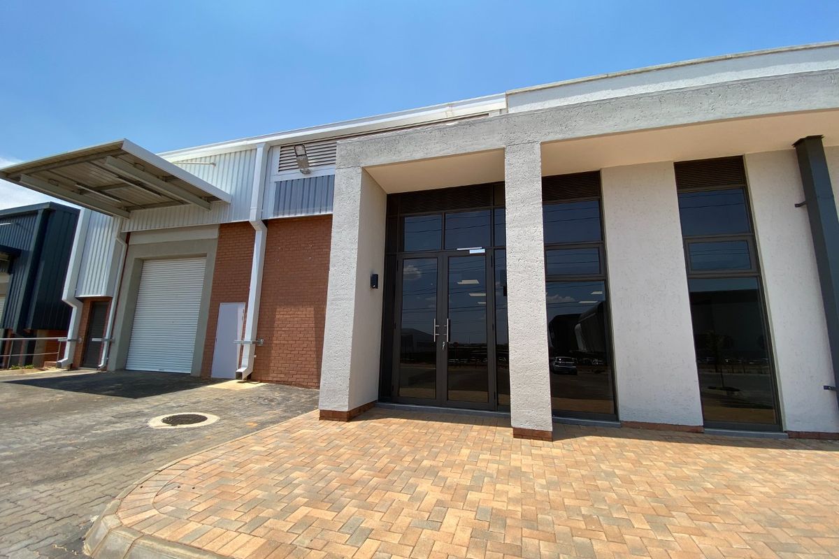 Modern industrial unit exterior featuring a paved entrance, glass facade, and a dedicated loading bay with a roller shutter door and canopy.