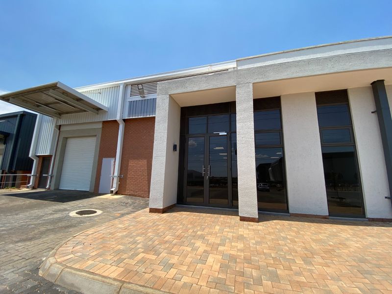 Modern industrial unit exterior featuring a paved entrance, glass facade, and a dedicated loading bay with a roller shutter door and canopy.