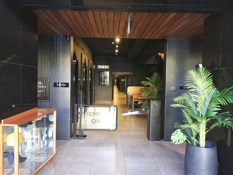 Modern apartment building entrance lobby featuring a security turnstile, tiled flooring, and a decorative slatted timber ceiling with recessed lighting.