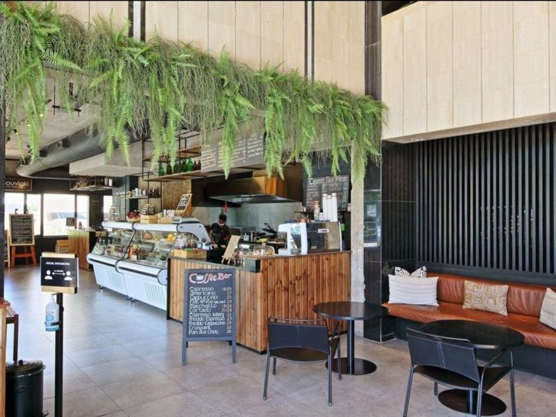 A modern commercial coffee bar area featuring stone wall cladding, slatted timber accents, and tiled flooring, suitable for a high-traffic apartment building lobby.