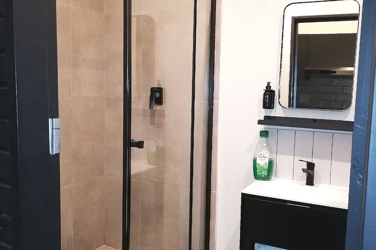 Modern bathroom featuring a walk-in shower with black-framed glass enclosure, wall-mounted vanity with basin, and contemporary tiled finishes.