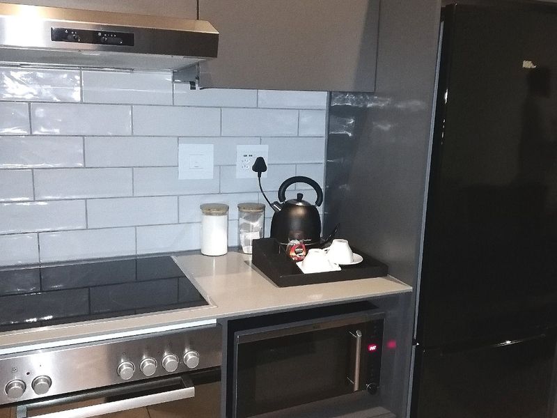 Modern kitchen featuring sleek grey cabinetry, subway tile backsplash, stone countertops, and integrated stainless steel appliances including an oven, cooktop, and microwave.