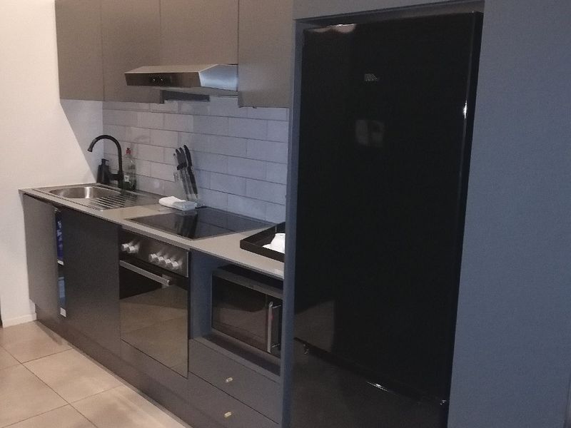 Modern kitchen featuring sleek dark cabinetry, integrated appliances, subway tile backsplash, and durable tiled flooring in a compact, efficient layout.