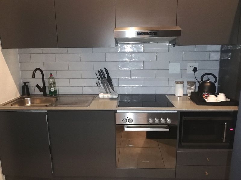 Modern compact kitchen featuring dark cabinetry, subway tile backsplash, stainless steel sink, and integrated appliances including an oven, hob, and microwave.