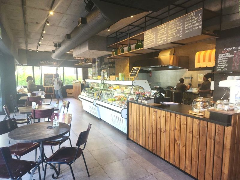 A commercial open-plan cafe space featuring industrial-style exposed ducting, a service counter with display refrigeration, and tiled flooring throughout.