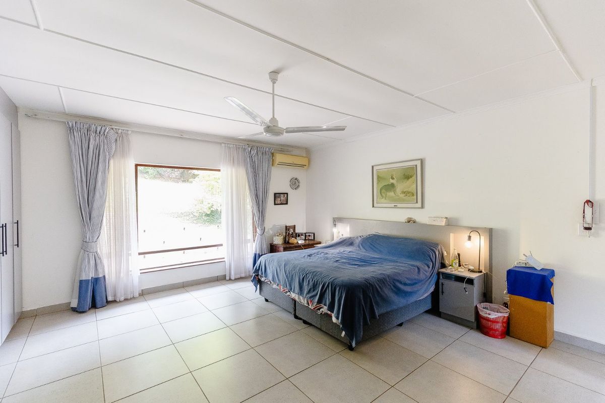 Spacious bedroom featuring large windows, tiled flooring, a ceiling fan, and a wall-mounted air conditioning unit.