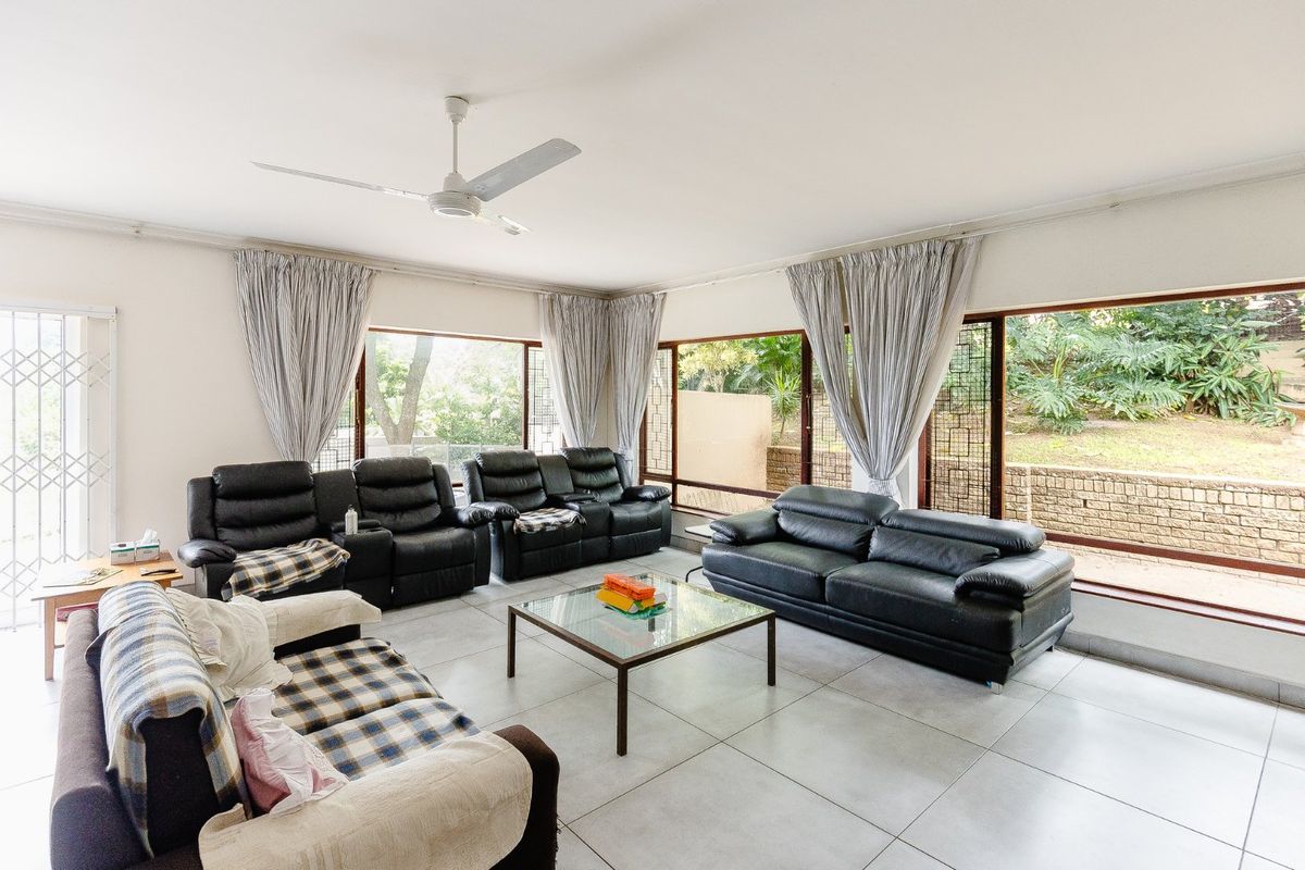 Spacious living room featuring large windows with garden views, tiled flooring, and a ceiling fan.