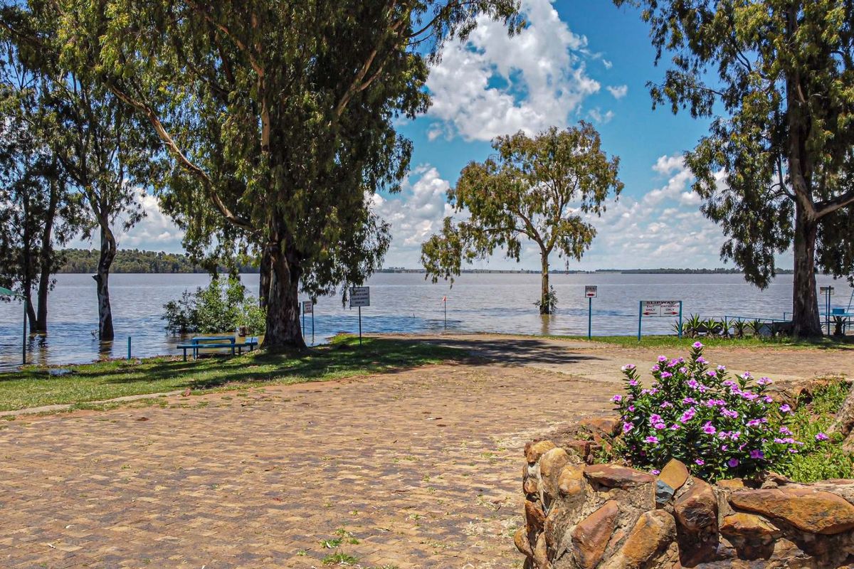 A scenic view of a waterfront property featuring a paved driveway, stone retaining wall, and mature trees overlooking the lake.