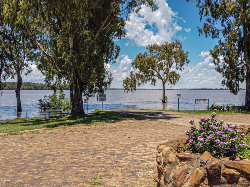 A scenic view of a waterfront property featuring a paved driveway, stone retaining wall, and mature trees overlooking the lake.