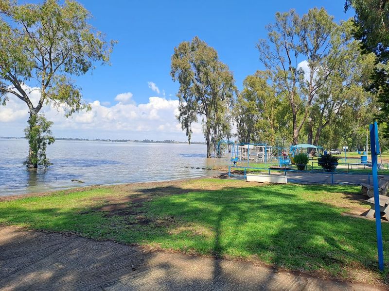 A scenic view of a large lakefront property featuring mature trees and expansive green lawn space.