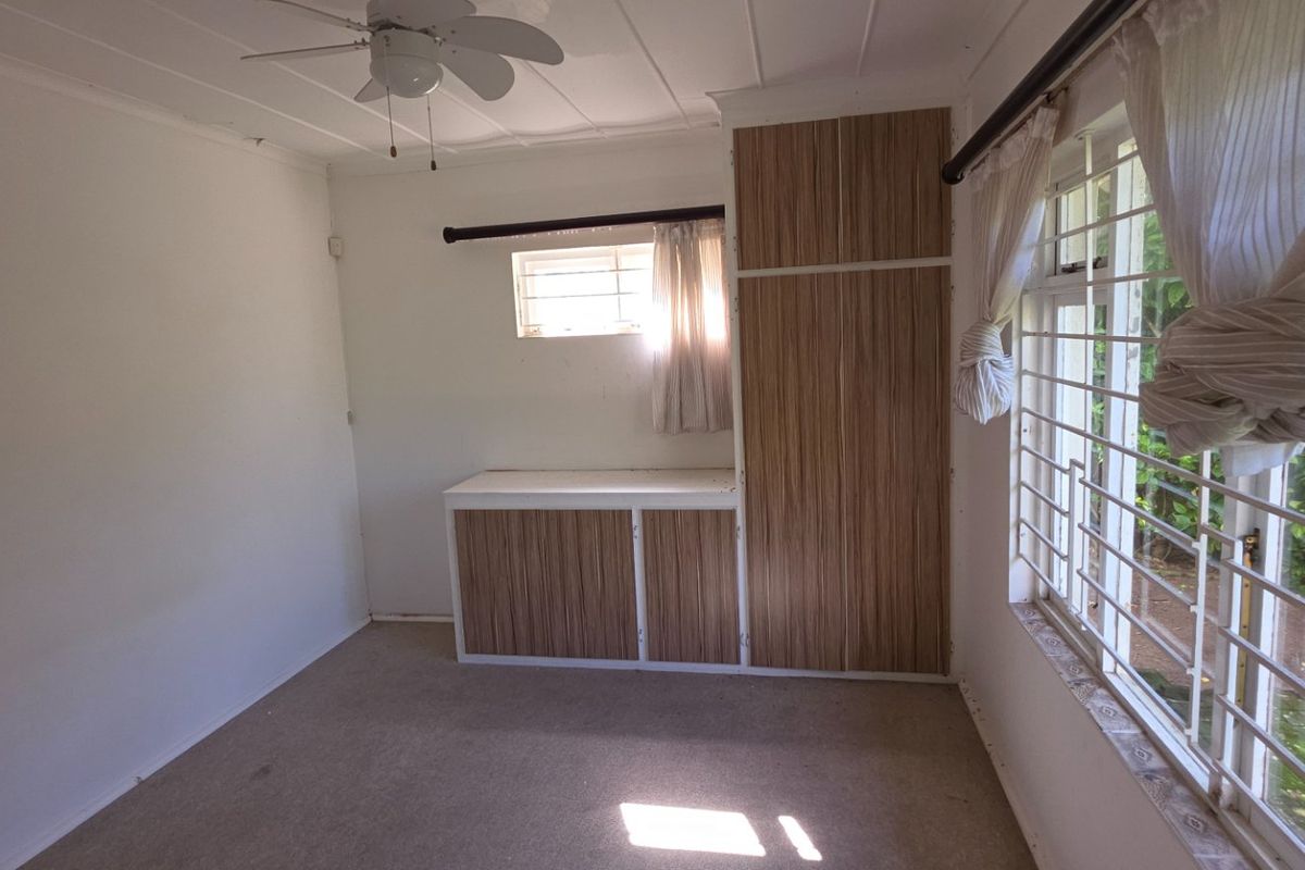A bedroom featuring built-in wooden cabinetry, a ceiling fan, and large windows with security bars, offering a functional and well-lit space.