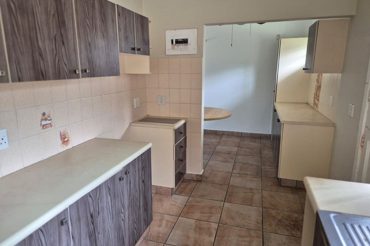 A dated kitchen featuring wood-grain laminate cabinetry, tiled splashbacks, and ceramic floor tiles, with an adjacent utility or dining area.