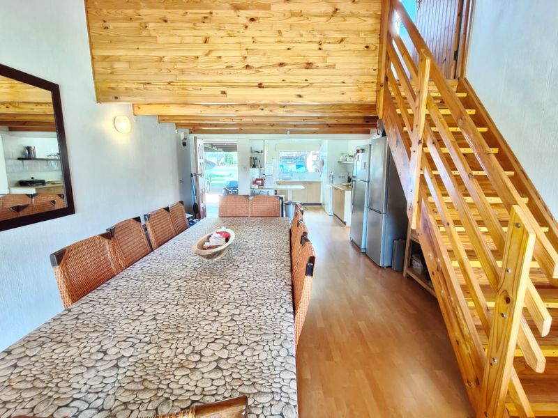 Open plan dining and kitchen area featuring a prominent timber staircase, wood-paneled ceiling, and laminate flooring, leading through to a functional kitchen space.