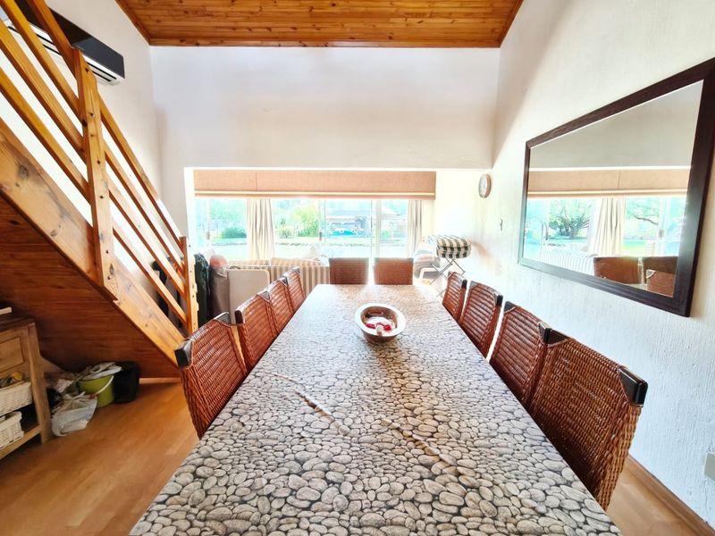 Spacious dining area featuring a timber staircase, vaulted timber ceiling, and large windows providing natural light and garden views.
