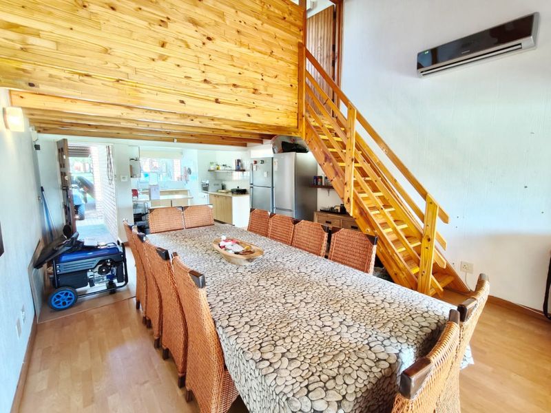 Open-plan living and dining area featuring a timber staircase, exposed wood ceiling, and integrated kitchen space with laminate flooring and air conditioning.