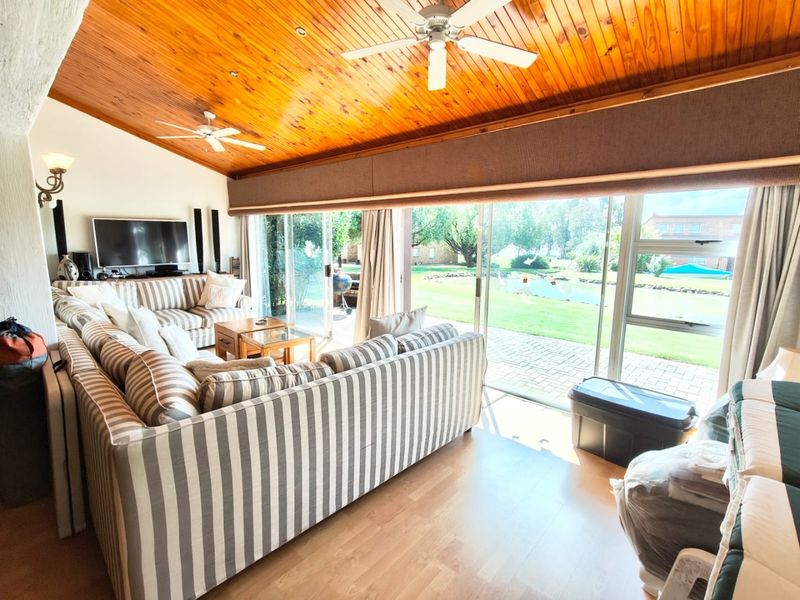 Spacious living room featuring a vaulted timber-clad ceiling, ceiling fans, and large sliding glass doors providing direct access to the garden and patio area.