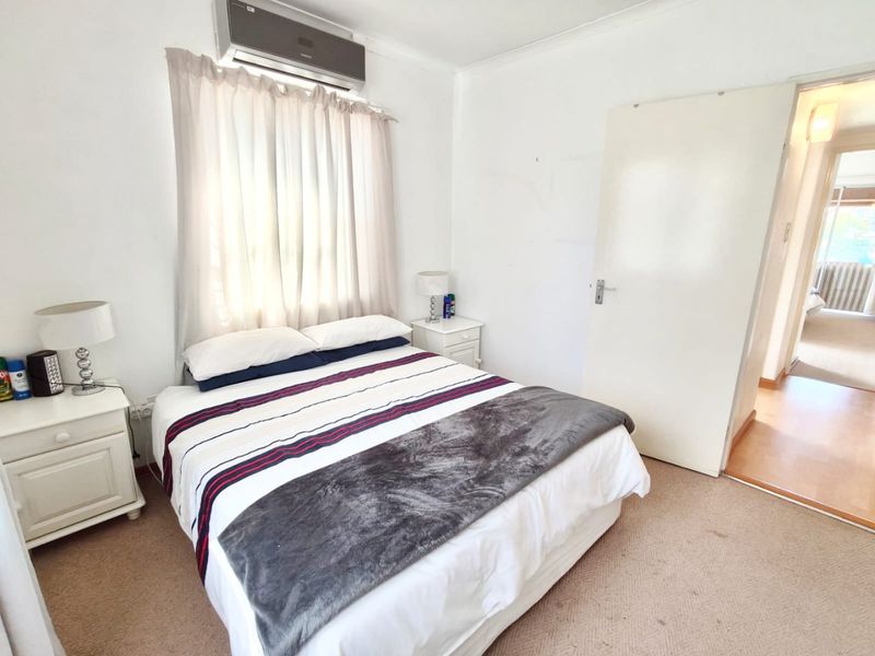 A functional bedroom featuring carpeted flooring, a wall-mounted air conditioning unit, and direct access to the hallway.