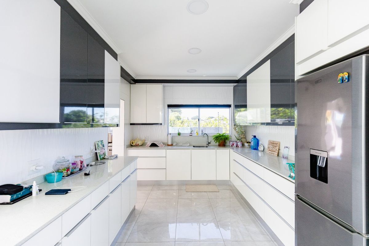 Modern galley-style kitchen featuring high-gloss cabinetry, stone countertops, tiled flooring, and integrated lighting, offering a clean and functional workspace.