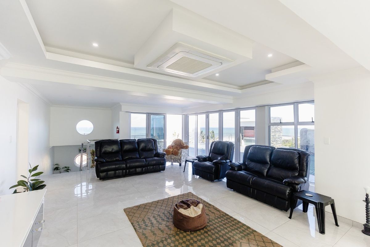 Spacious living area featuring high-gloss tiled flooring, recessed ceiling detail with integrated air conditioning, and expansive glass doors offering natural light and coastal views.