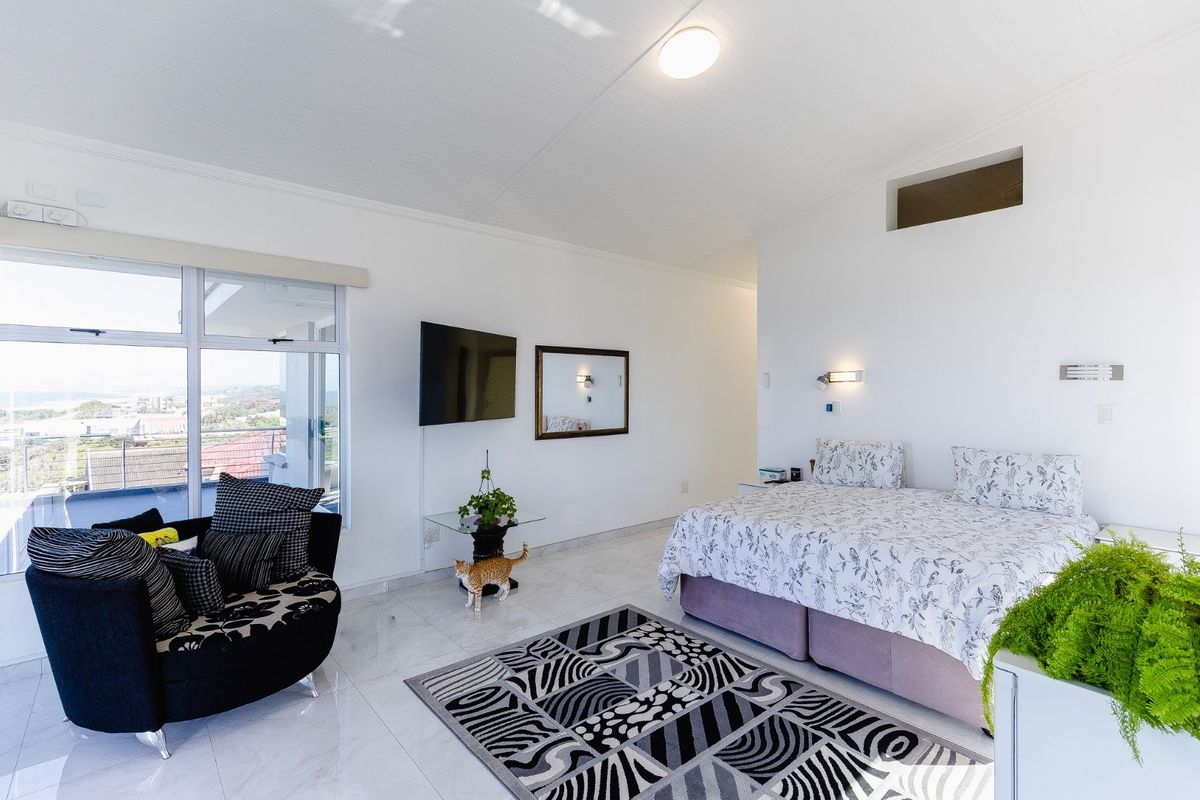 A bright bedroom featuring tiled flooring, wall-mounted lighting, and a large sliding glass door providing access to an outdoor area with scenic views.