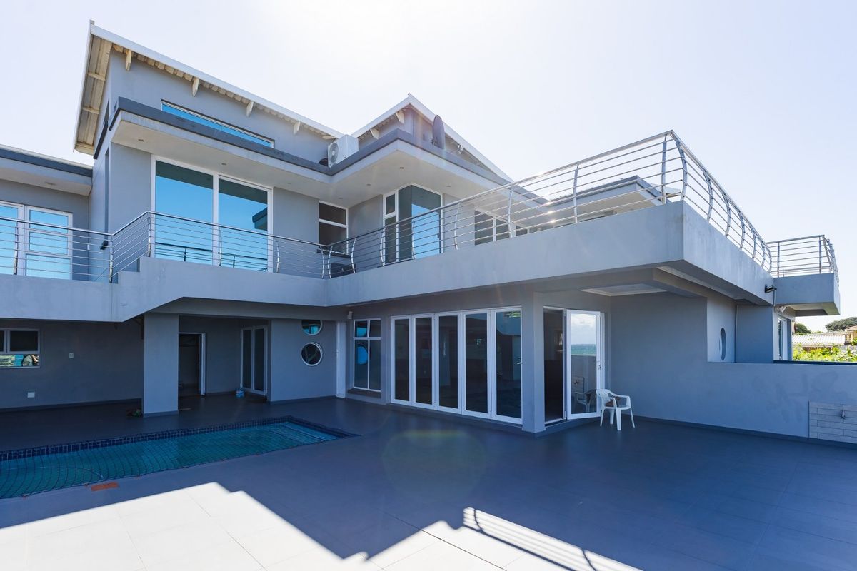 Rear exterior view featuring a spacious tiled patio, swimming pool, and a large upper-level balcony with modern stainless steel railings.