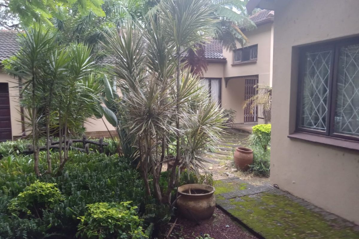 A view of the rear garden area featuring a paved walkway, mature landscaping, and leaded glass windows on the exterior facade.