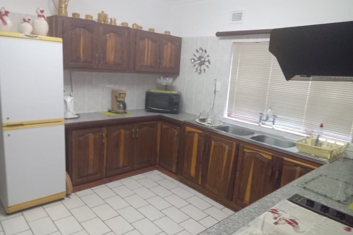 A functional kitchen featuring wooden cabinetry, tiled flooring, a double basin sink, and a built-in extractor fan.
