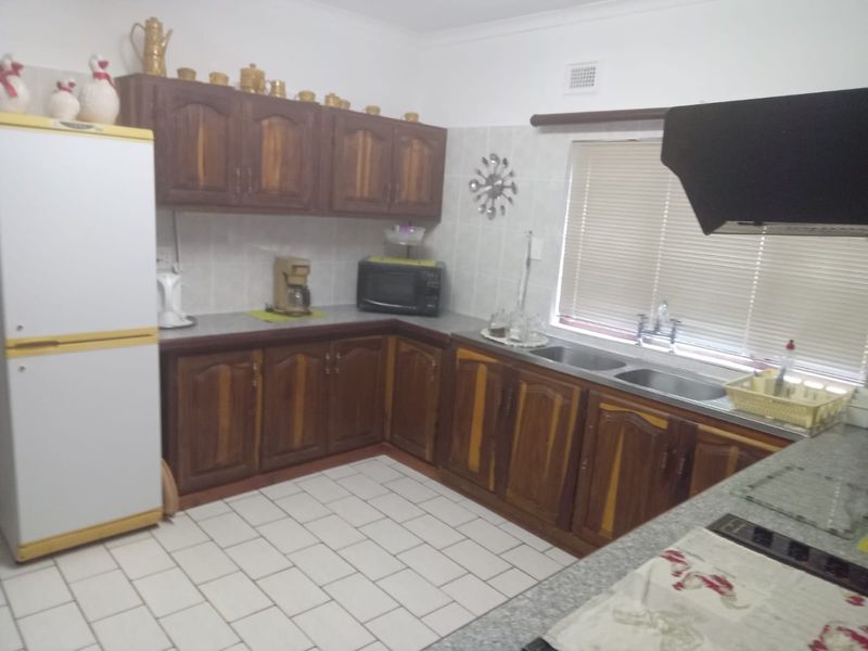 A functional kitchen featuring wooden cabinetry, tiled flooring, a double basin sink, and a built-in extractor fan.