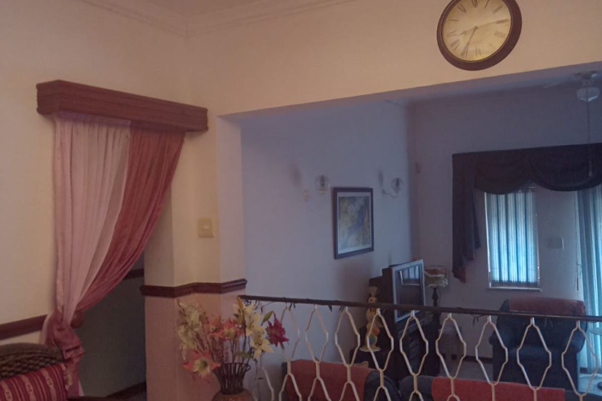 A split-level living area featuring tiled flooring, a decorative metal balustrade, and an ornate chandelier, providing a traditional layout with distinct living zones.