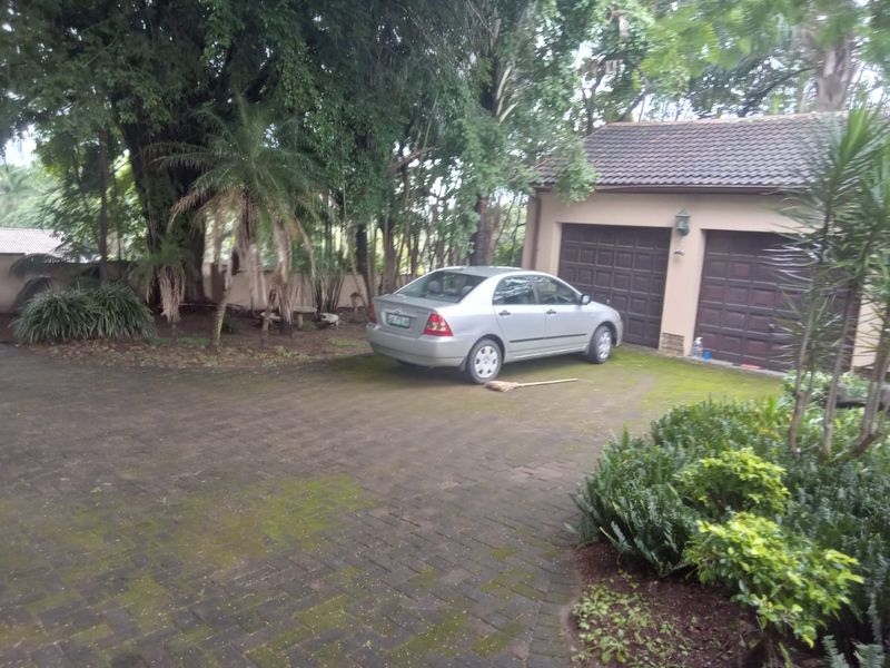 Front exterior view showing a double garage with a paved driveway and mature garden surroundings.