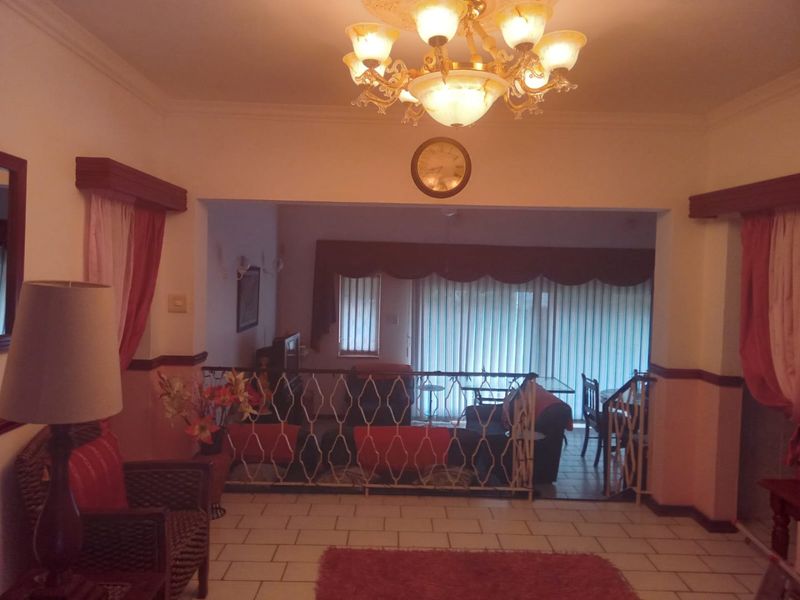 Open plan living area featuring tiled floors, an ornate chandelier, and a wrought iron balustrade separating the split-level space.