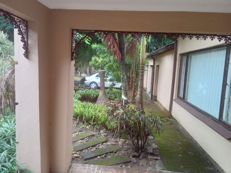 A covered patio area featuring decorative wrought iron brackets, overlooking a lush garden with a paved walkway and established greenery.