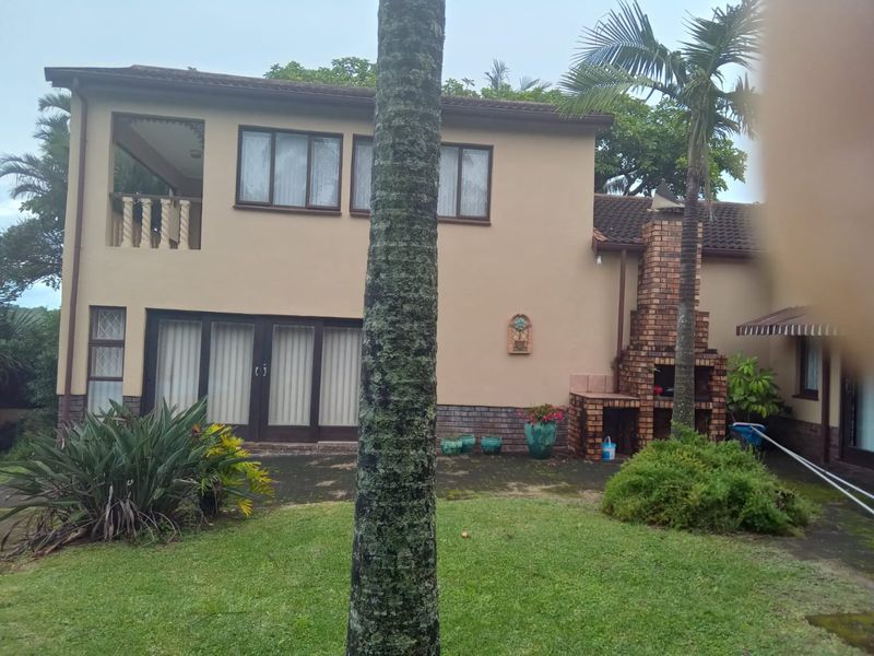 Rear view of a two-story house featuring a brick outdoor fireplace, a balcony, and a paved patio area leading to a garden.