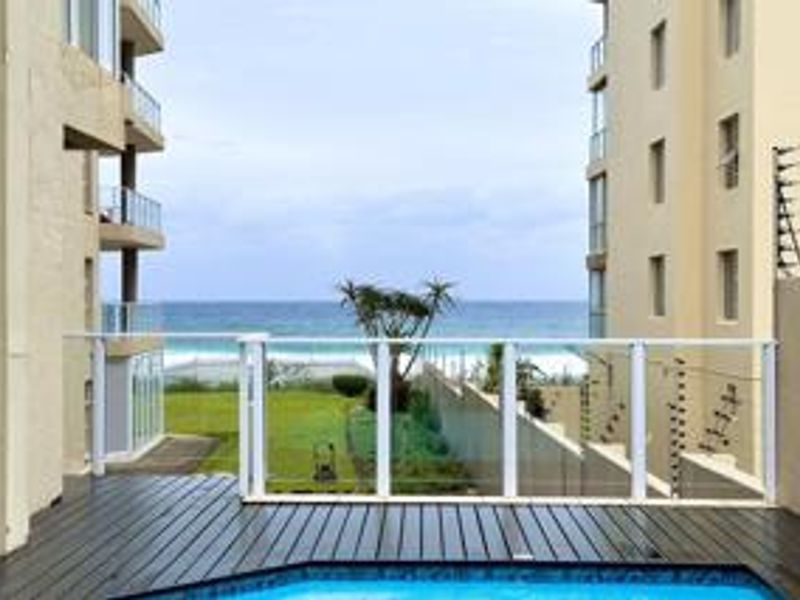 A well-maintained pool area featuring timber decking and a glass balustrade, offering a clear view of the ocean and surrounding coastal landscape.