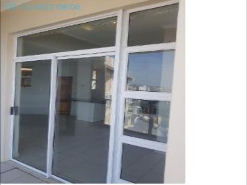 A view of a balcony or patio area featuring white aluminium sliding doors and fixed glass panels, providing access to the interior living space.