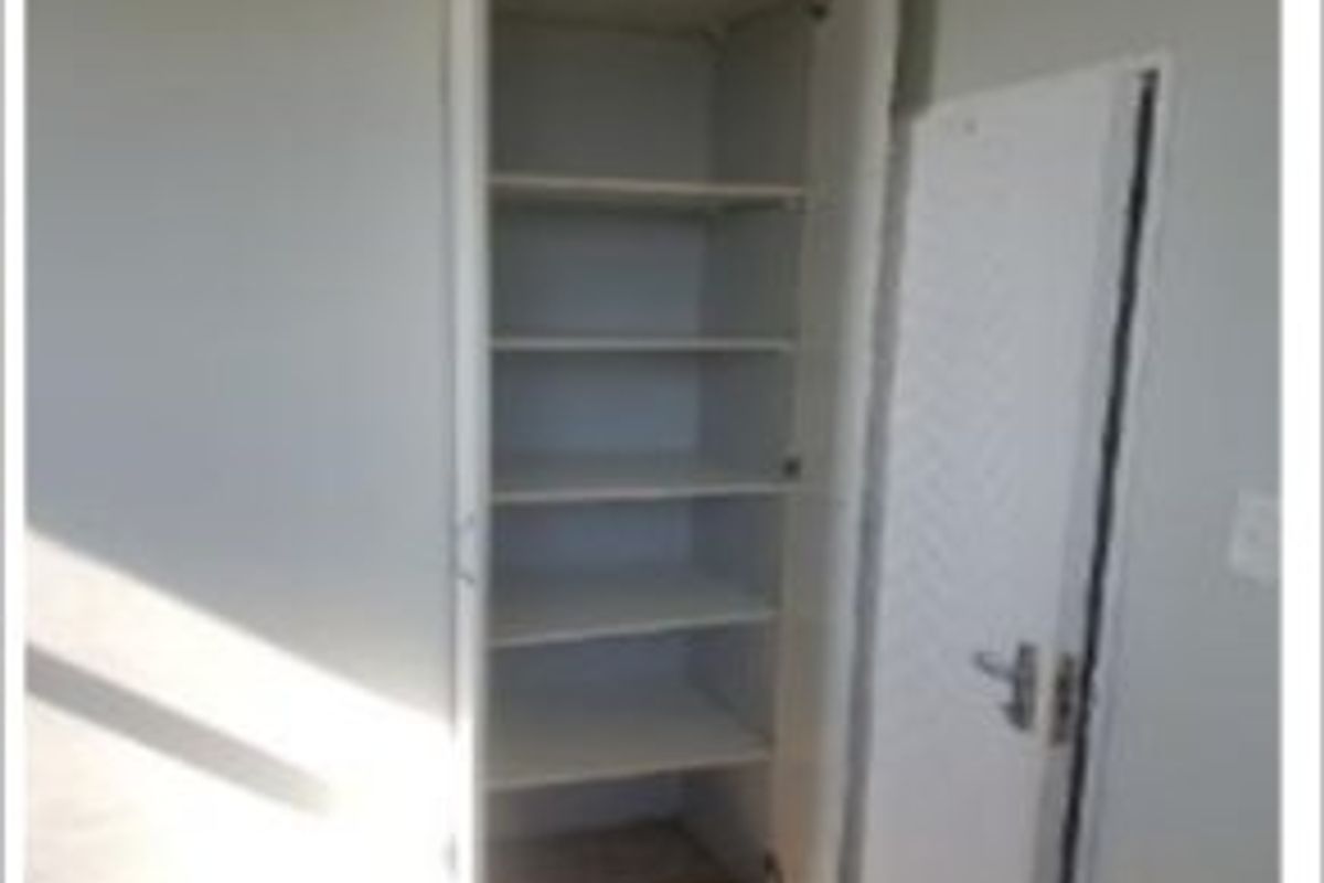 A bedroom interior featuring a built-in storage cupboard with open shelving and a standard internal door.