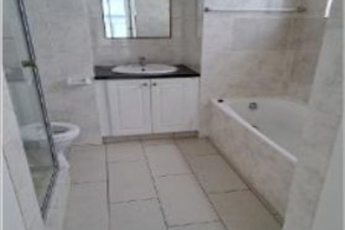 A functional bathroom featuring a vanity with basin, a separate bathtub, a glass-enclosed shower, and neutral wall and floor tiling throughout.