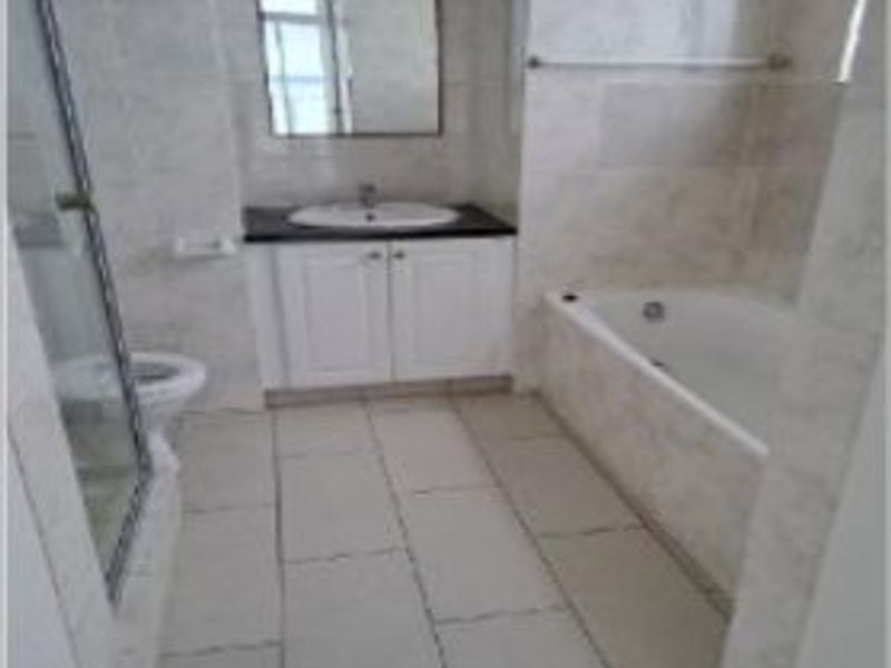 A functional bathroom featuring a vanity with basin, a separate bathtub, a glass-enclosed shower, and neutral wall and floor tiling throughout.