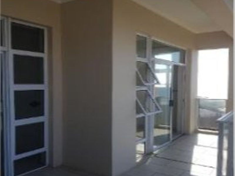 A covered balcony area featuring tiled flooring, aluminium-framed glass doors, and a balustrade, providing an outdoor space accessible from the apartment interior.