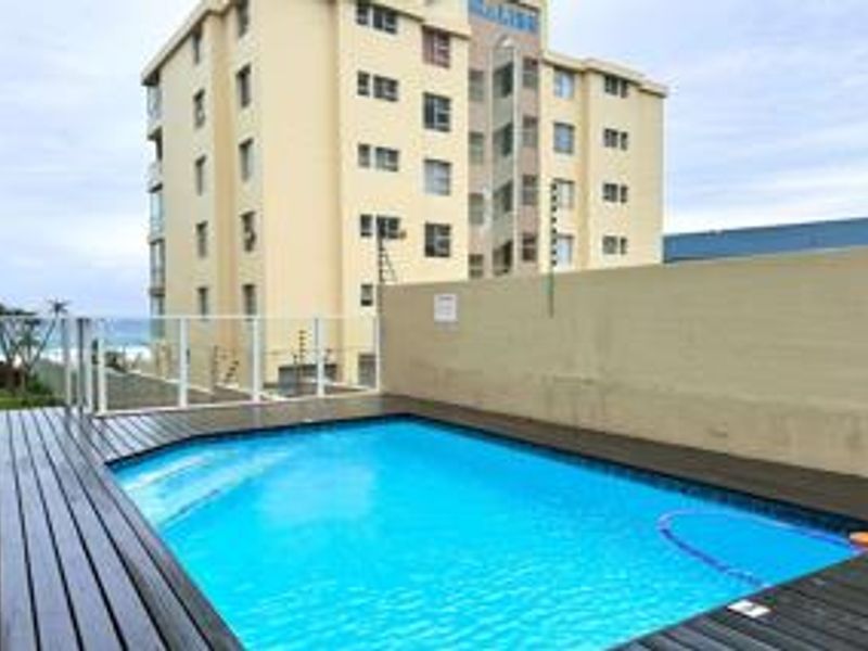 A well-maintained outdoor swimming pool area featuring timber decking, glass balustrades, and secure boundary walls with electric fencing.