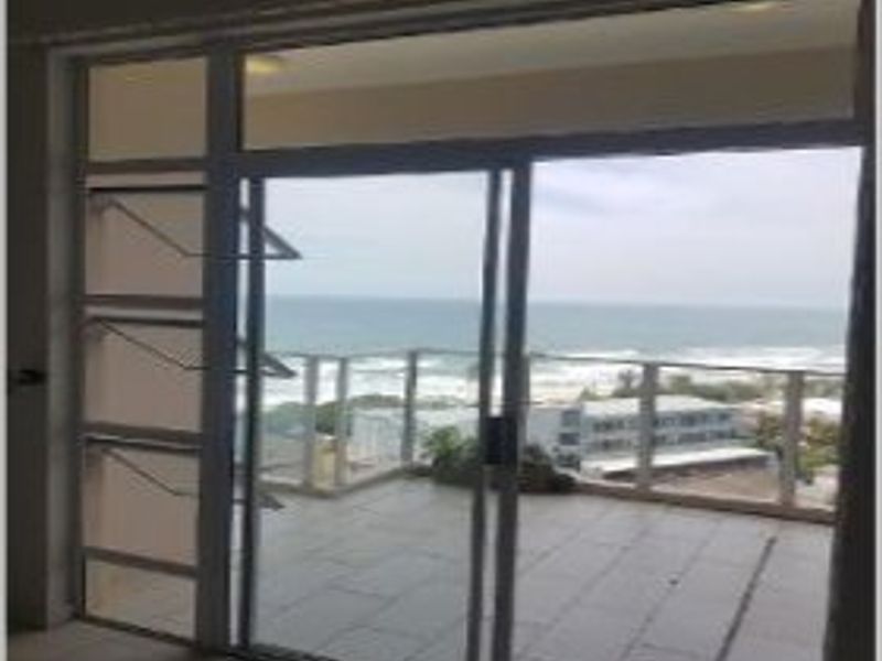 A spacious balcony featuring tiled flooring and a glass balustrade, offering expansive ocean views through large sliding glass doors.