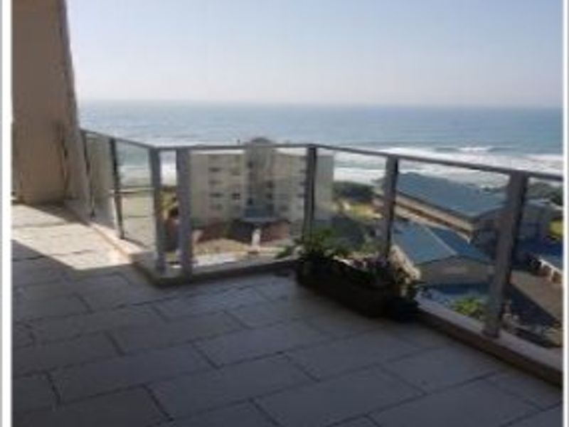 A spacious balcony featuring tiled flooring and a modern glass balustrade, offering expansive ocean and coastal views.