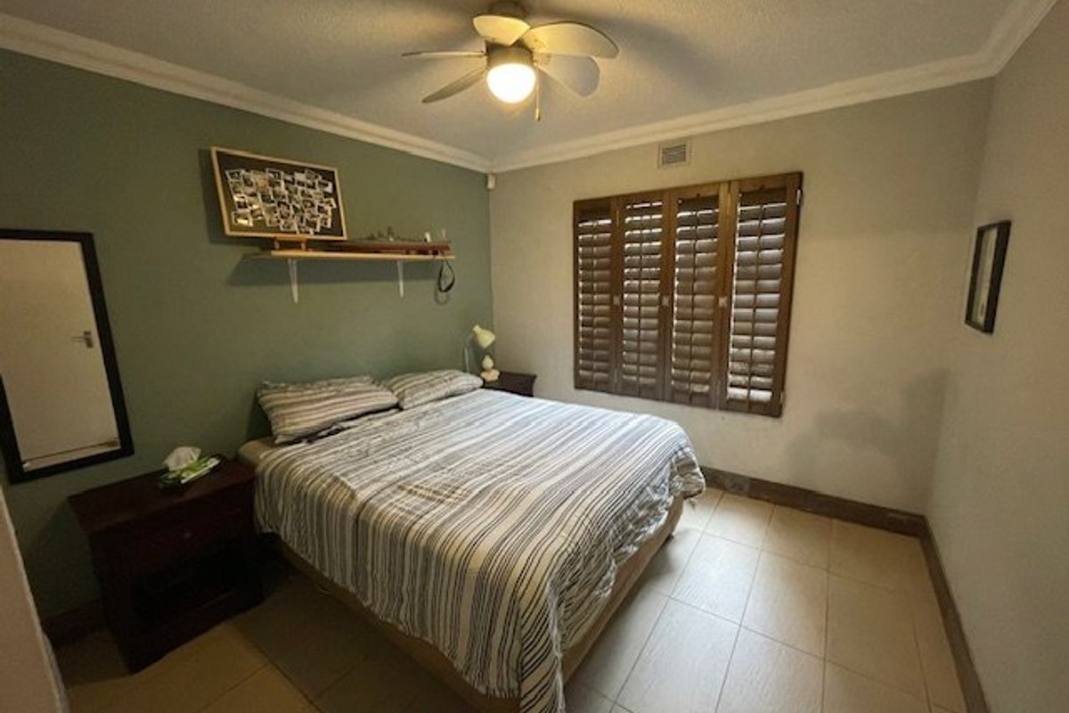 A bedroom featuring tiled flooring, a ceiling fan, and wooden shutters on the window, providing a functional and comfortable living space.